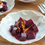Top view of three small white bowls of diced red beets. Two bowls with crumbled goat cheese and orange zest. One bowl with just orange zest is close up and in front.