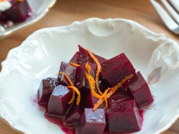 Top view of three small white bowls of diced red beets. Two bowls with crumbled goat cheese and orange zest. One bowl with just orange zest is close up and in front.