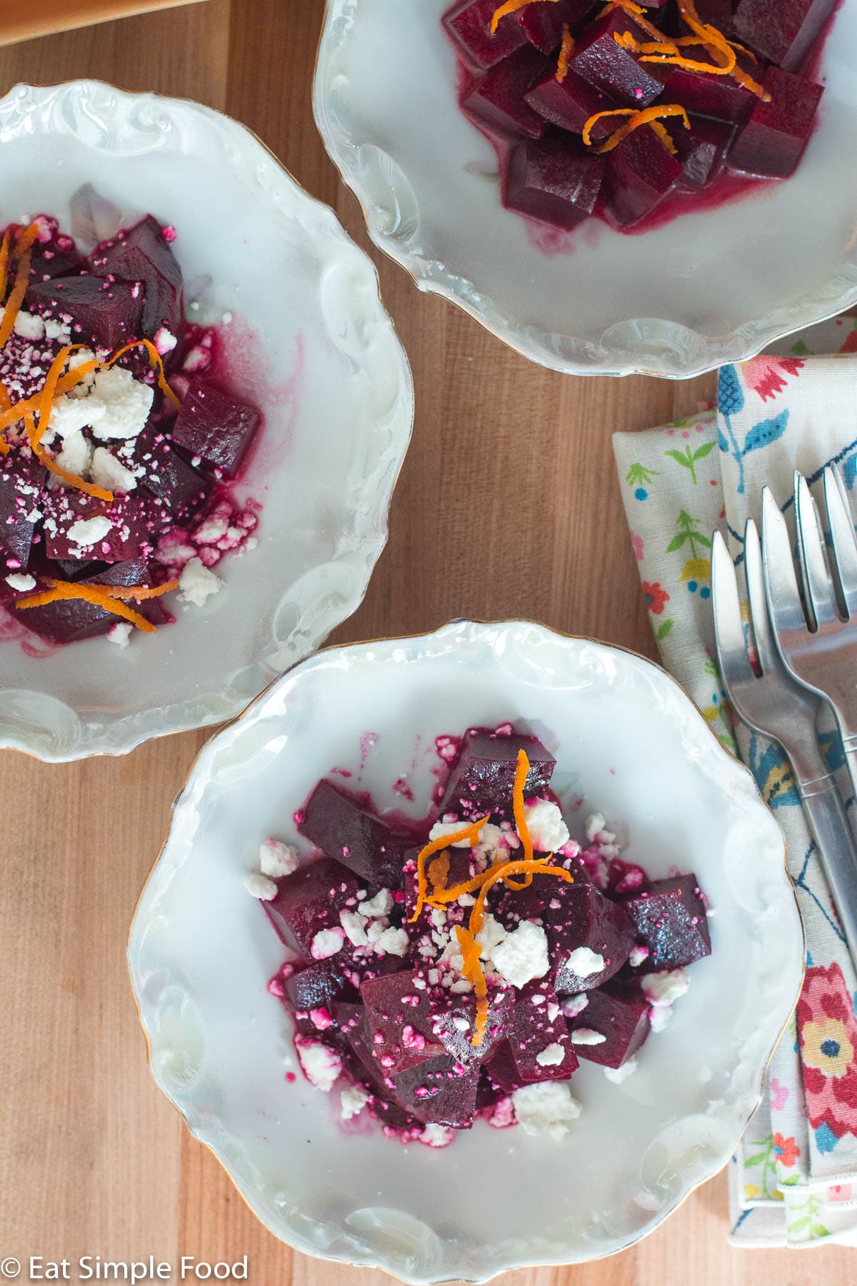 Top view of three small white bowls of diced red beets. Two bowls with crumbled goat cheese and orange zest. One bowl with just orange zest.