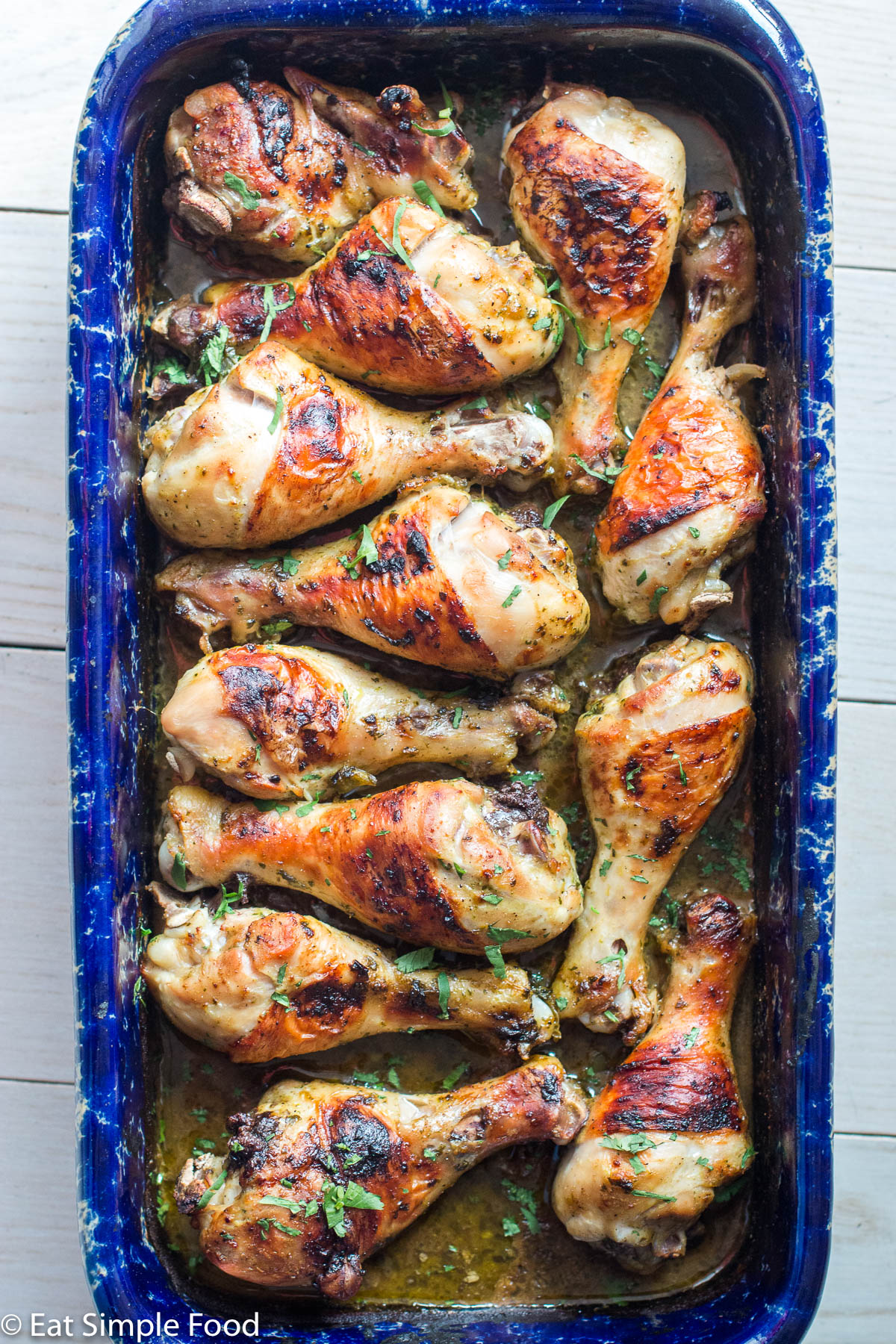 Brown Roasted Chicken legs in a cilantro sauce in a blue baking dish. Top view.