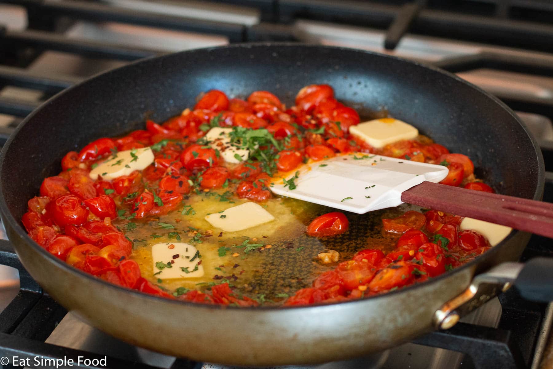 Skillet of fresh halved cherry tomatoes, butter, olive oil, and green herbs cooking in on the stovetop.