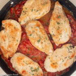 Close up of 6 browned chicken cutlets over a fresh cherry tomato sauce in a skillet. Top view.