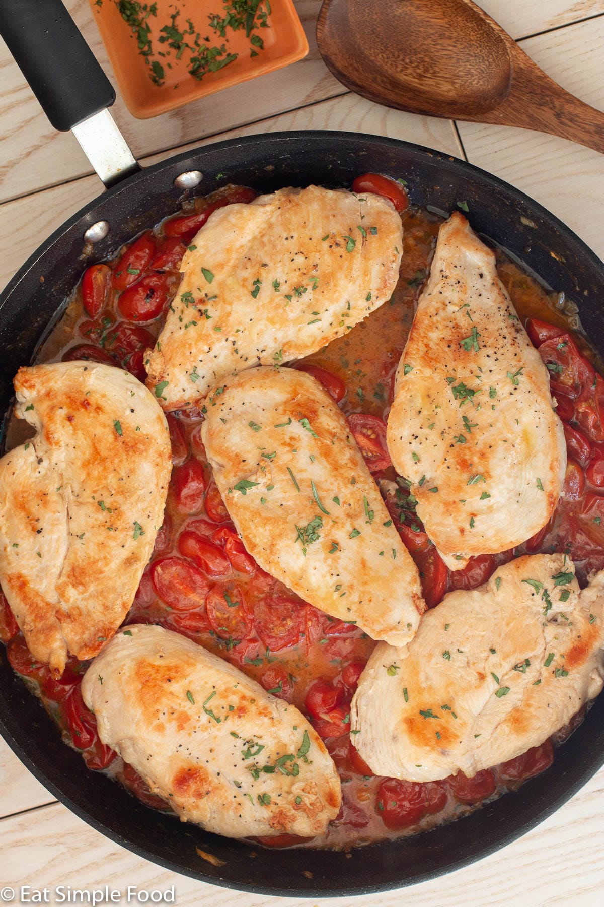 Top view of 6 browned chicken cutlets over a fresh cherry tomato sauce in a skillet.