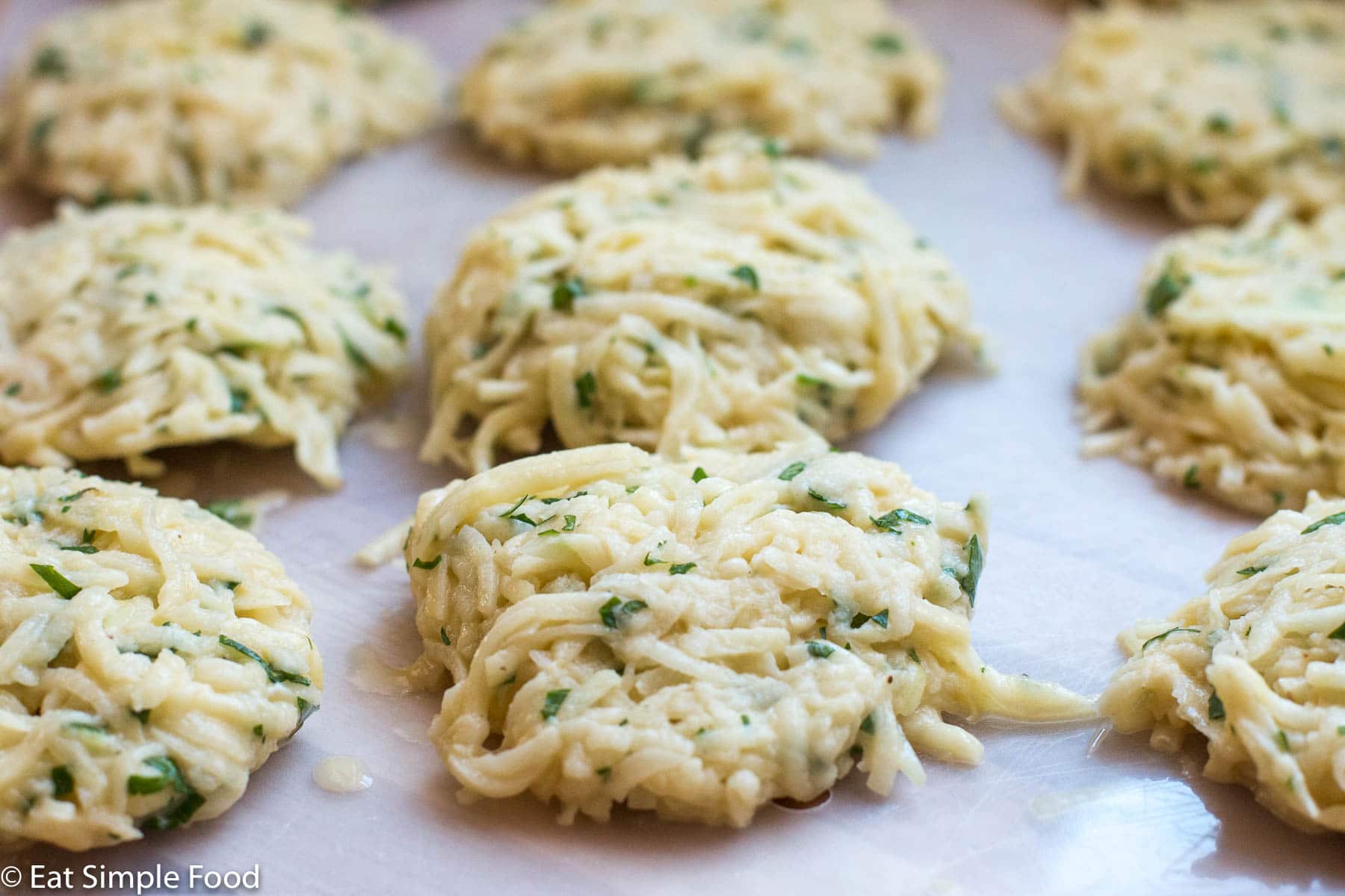 Close up side view of uncooked potato pancakes on a white cutting board.