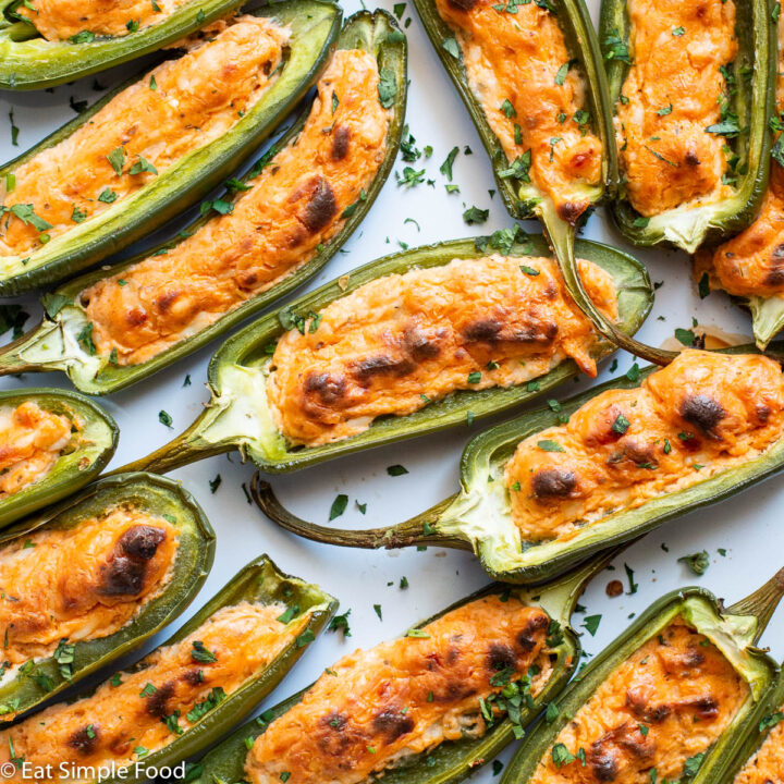 Close up ofcooked jalapeno poppers filled with a brown orange crust and a chopped cilantro garnish. Top view, close up.