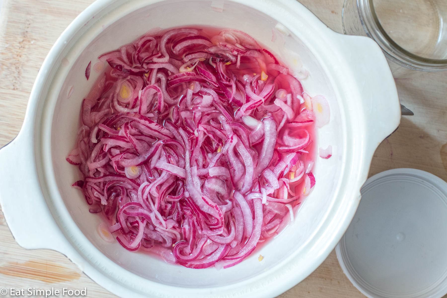Top view of sliced marinated (wilted) red onions in a white bowl.