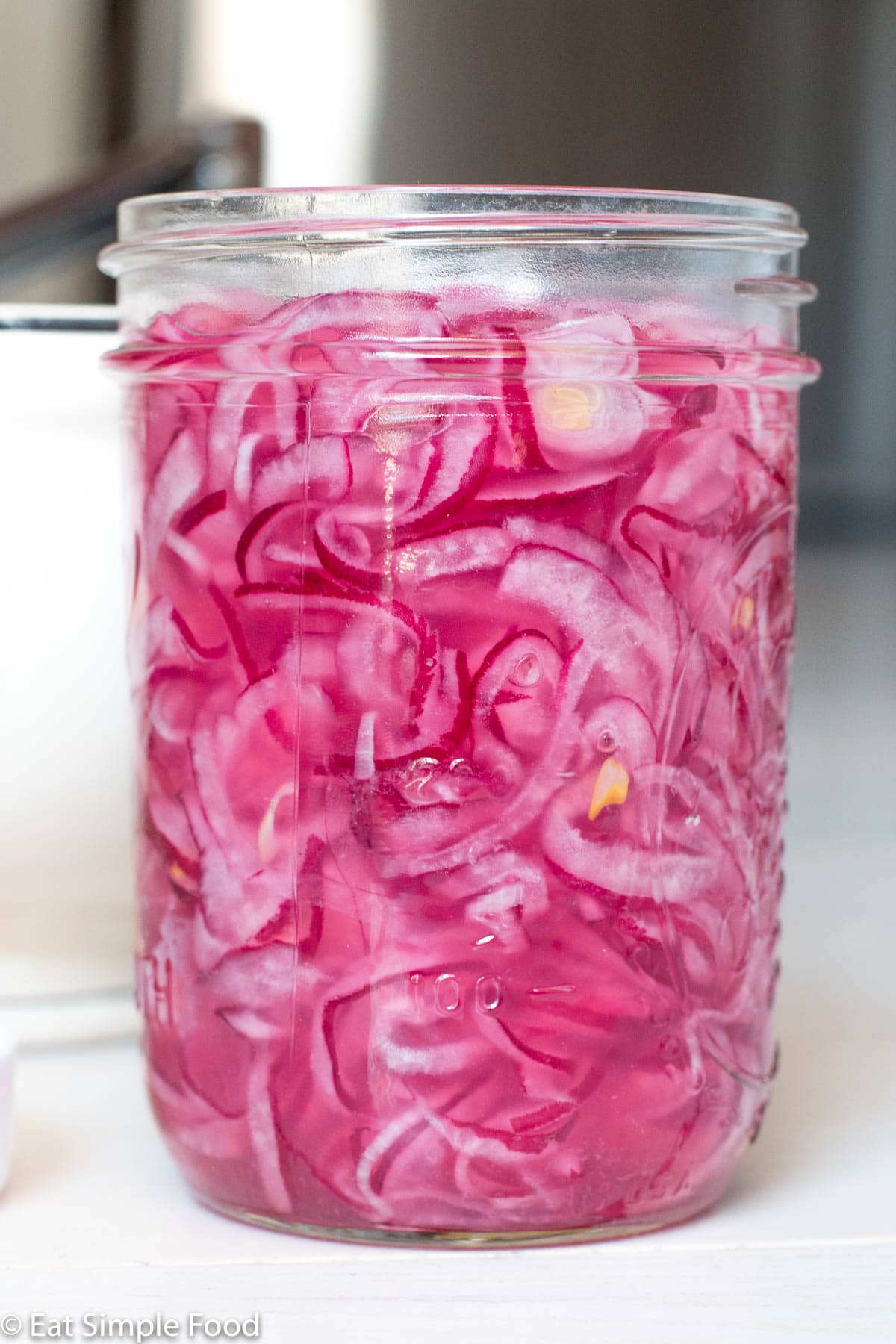 Side view of a clear pint jar of marinated sliced red onion in liquid.