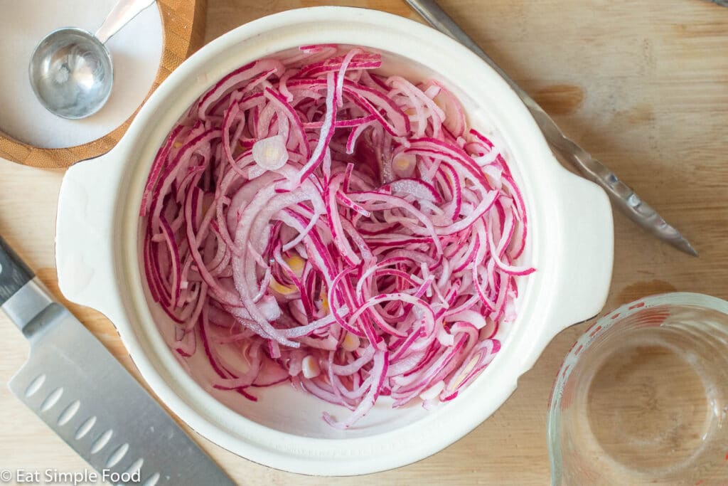 Top view of sliced red onions in a white bowl unmarinated.