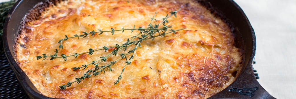 Scalloped Potatoes Cooked Golden Brown in Cast Iron Skillet with Thyme garnish. Side view.