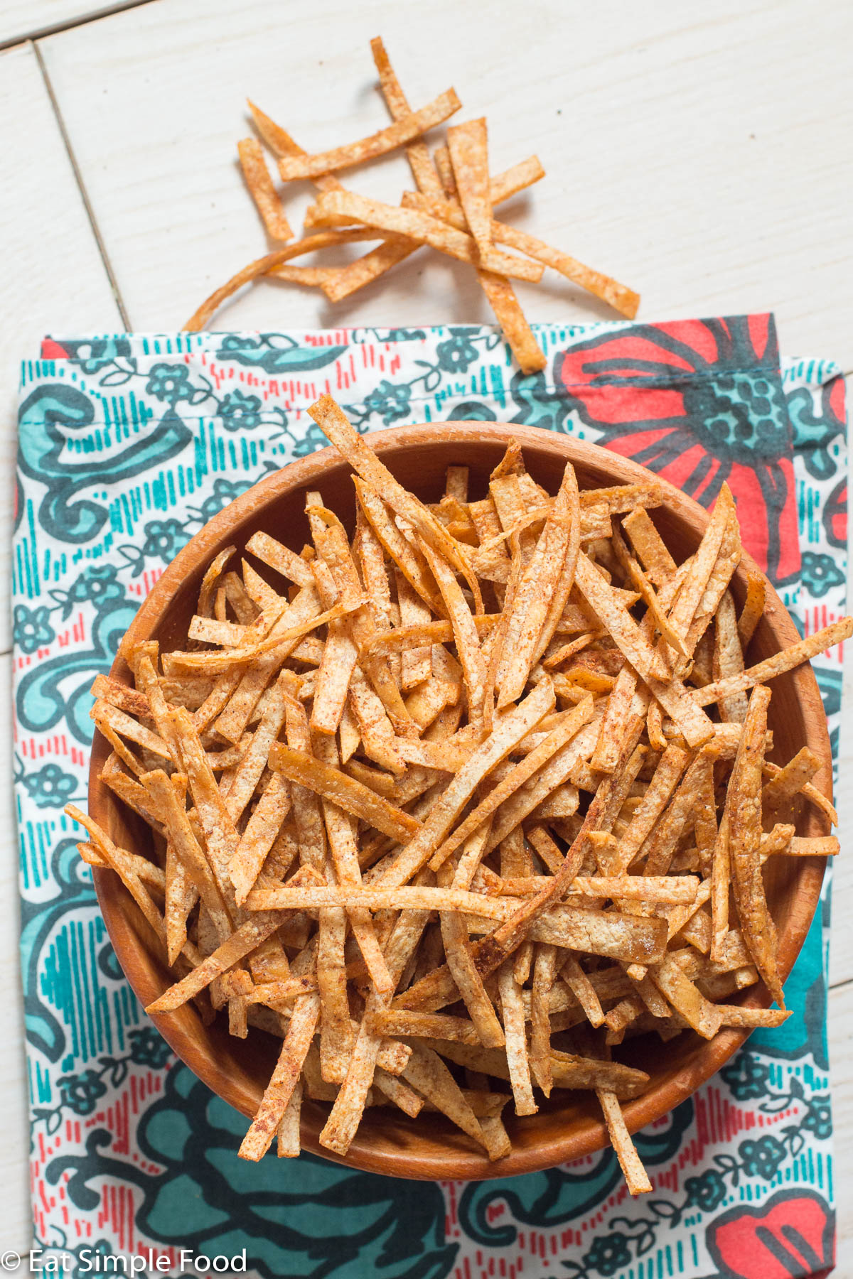 Crispy baked tortilla chips in a wood bowl over a colorful napkin. Top view.