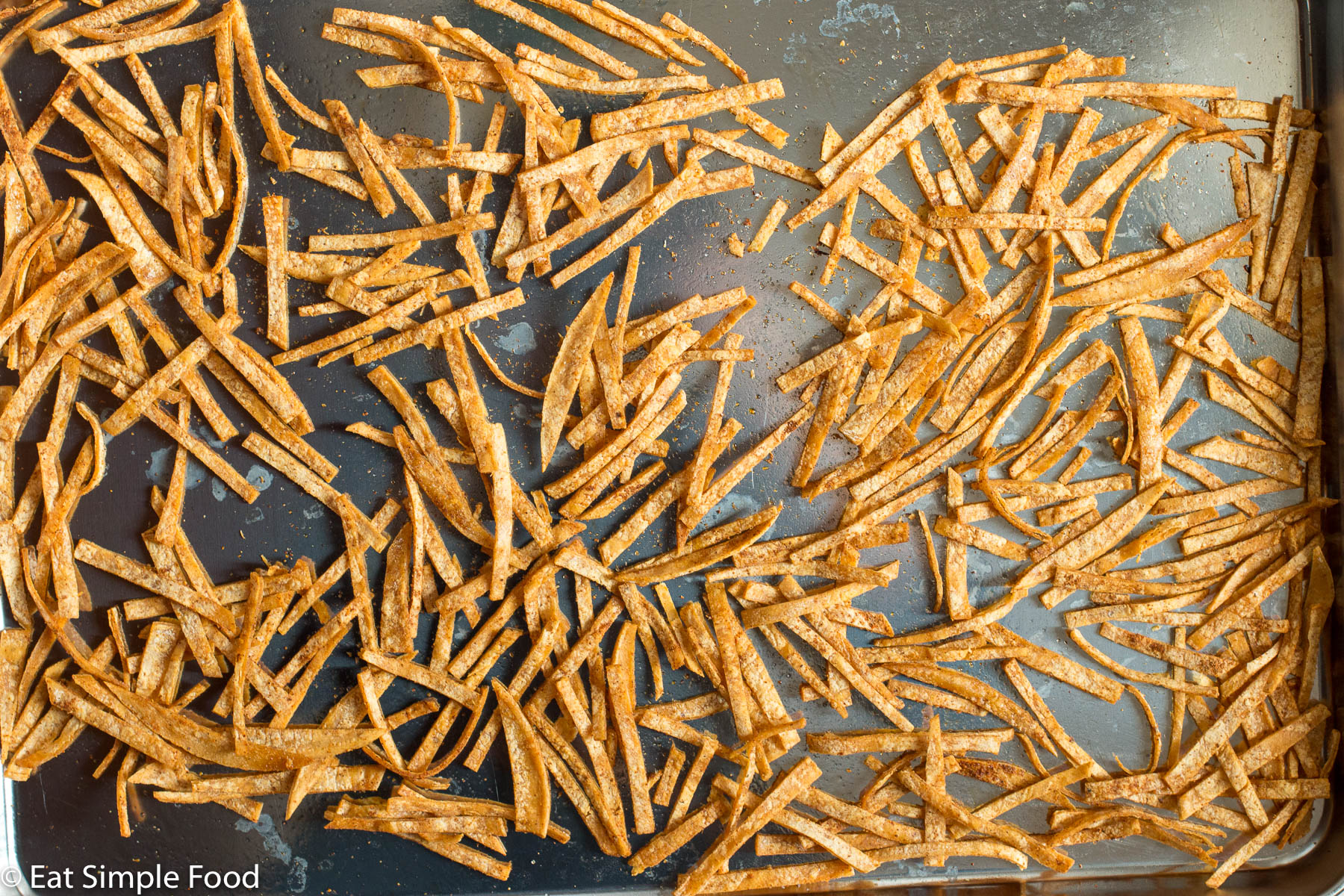 Cooked tortilla strips on a stainless steel sheet pan. Top view.
