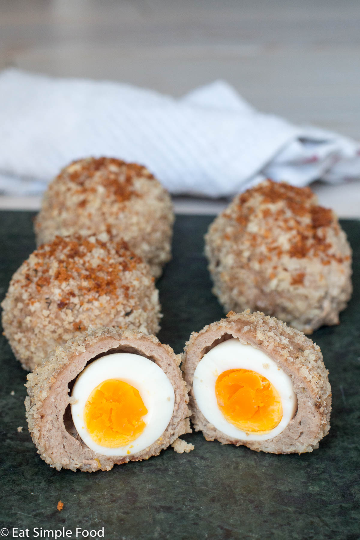 Side view of a cut open turkey scotch egg revealing a the egg and the egg yolk wrapped in cooked turkey and breadcrumbs.