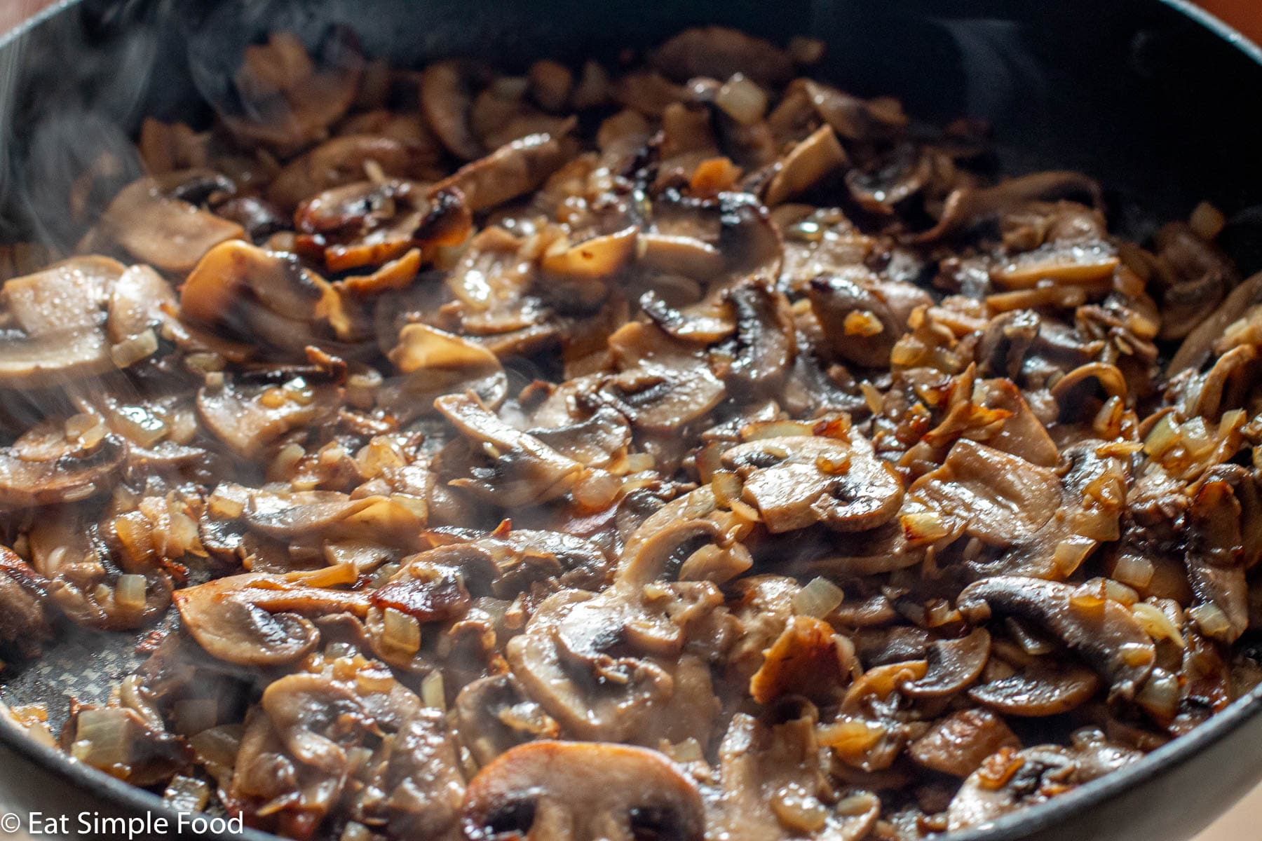 Black pan of sliced browned seared mushrooms with onions.