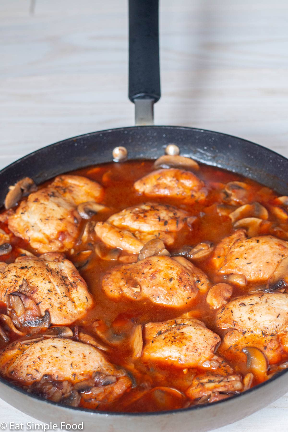 Black skillet with chicken thighs in a red brown mushroom based sauce. Side view.