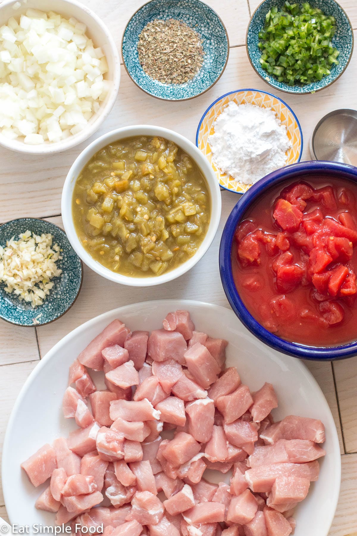 Ingredients: diced pork chop, bowl of canned diced tomatoes, bowl of green chiles, bowl of diced onions, and four small containers of minced garlic, cornstarch, dried oregano, and diced jalapeno.