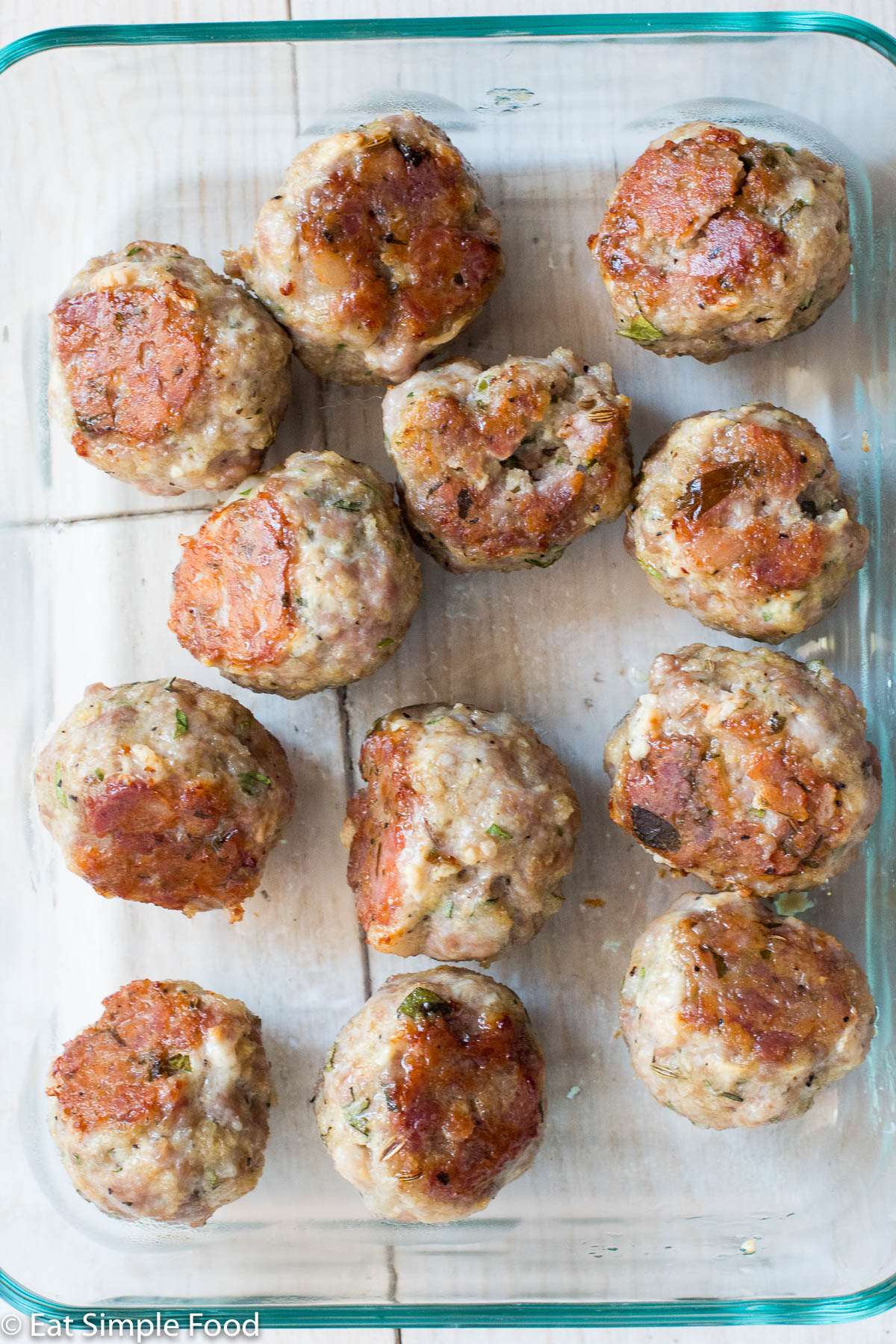 12 browned sausage meatballs in a clear glass rectangle pyrex on a white wood table.