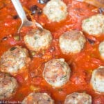 Browned sausage meatballs in a tomato sauce with olives and capers. Close up.