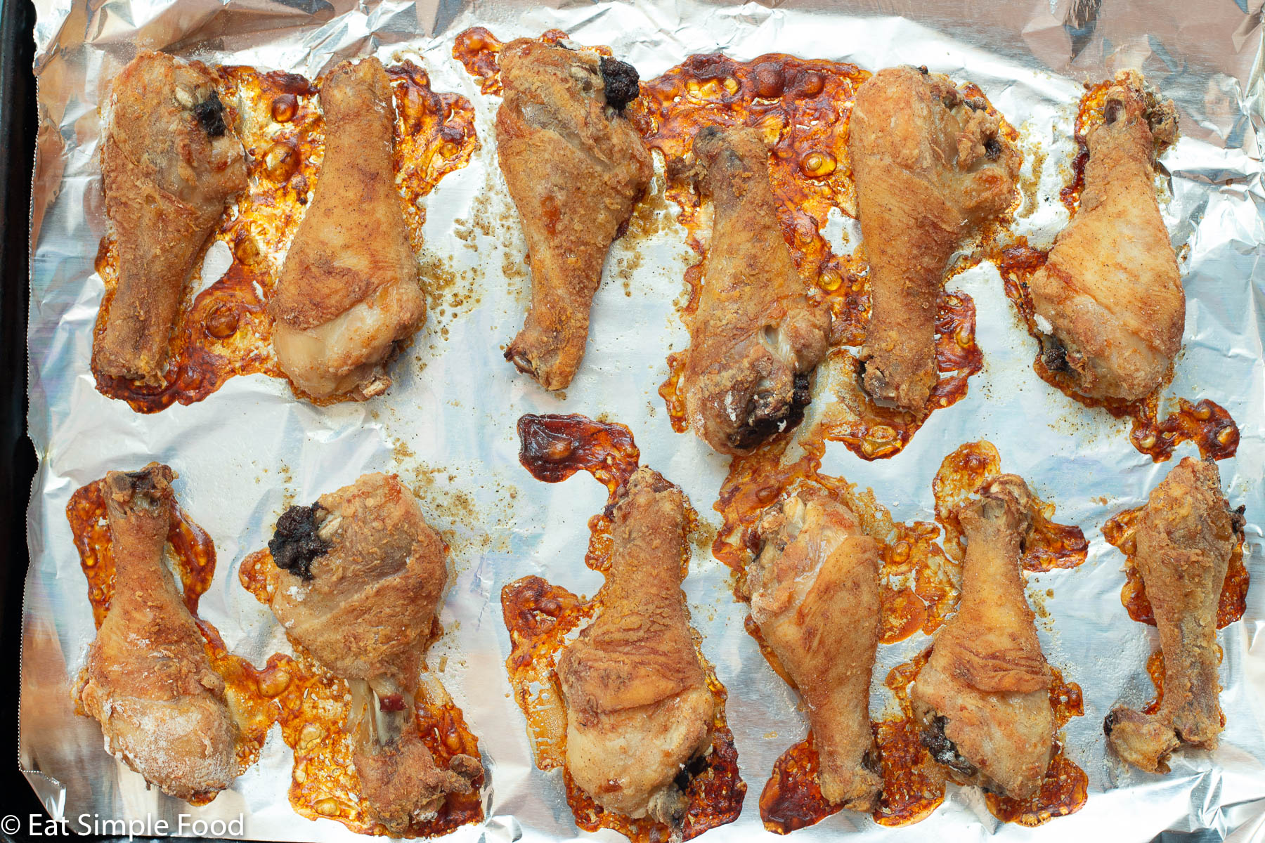 12 Baked Chicken drumsticks on an aluminum covered baking sheet. Top view.