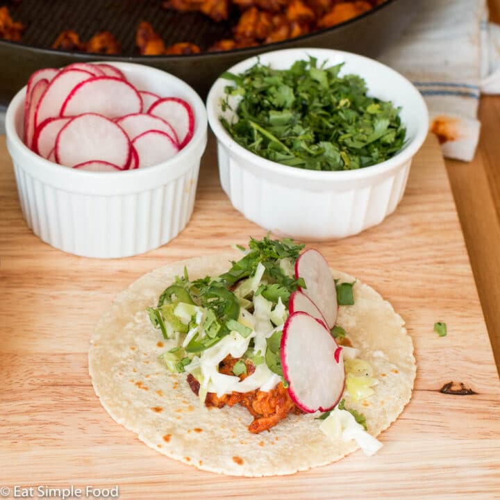 One taco filled with chicken, cole slaw, cilantro, sliced jalapenos, and 3 sliced radishes. Ingredients in background.