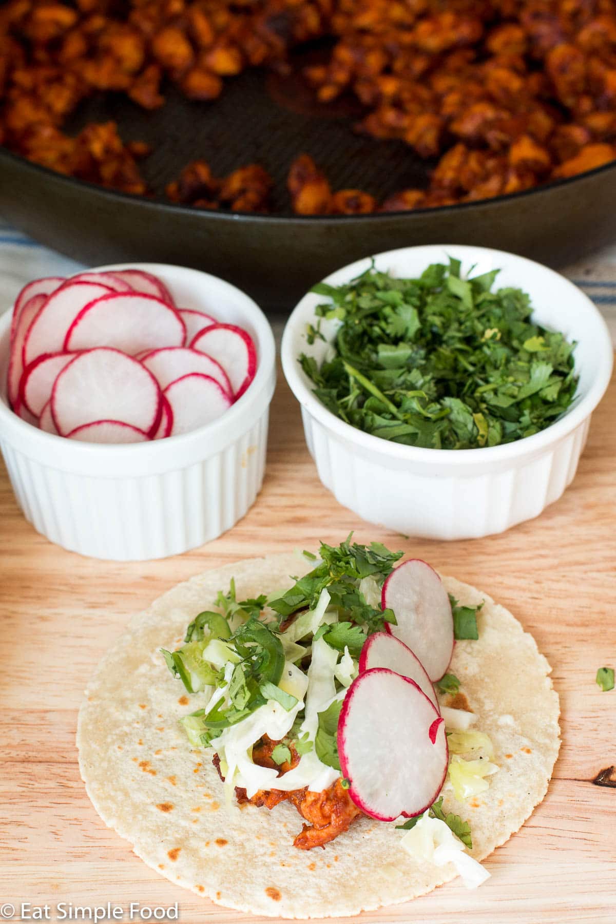 One taco filled with chicken, cole slaw, cilantro, sliced jalapenos, and 3 sliced radishes. Ingredients in background.