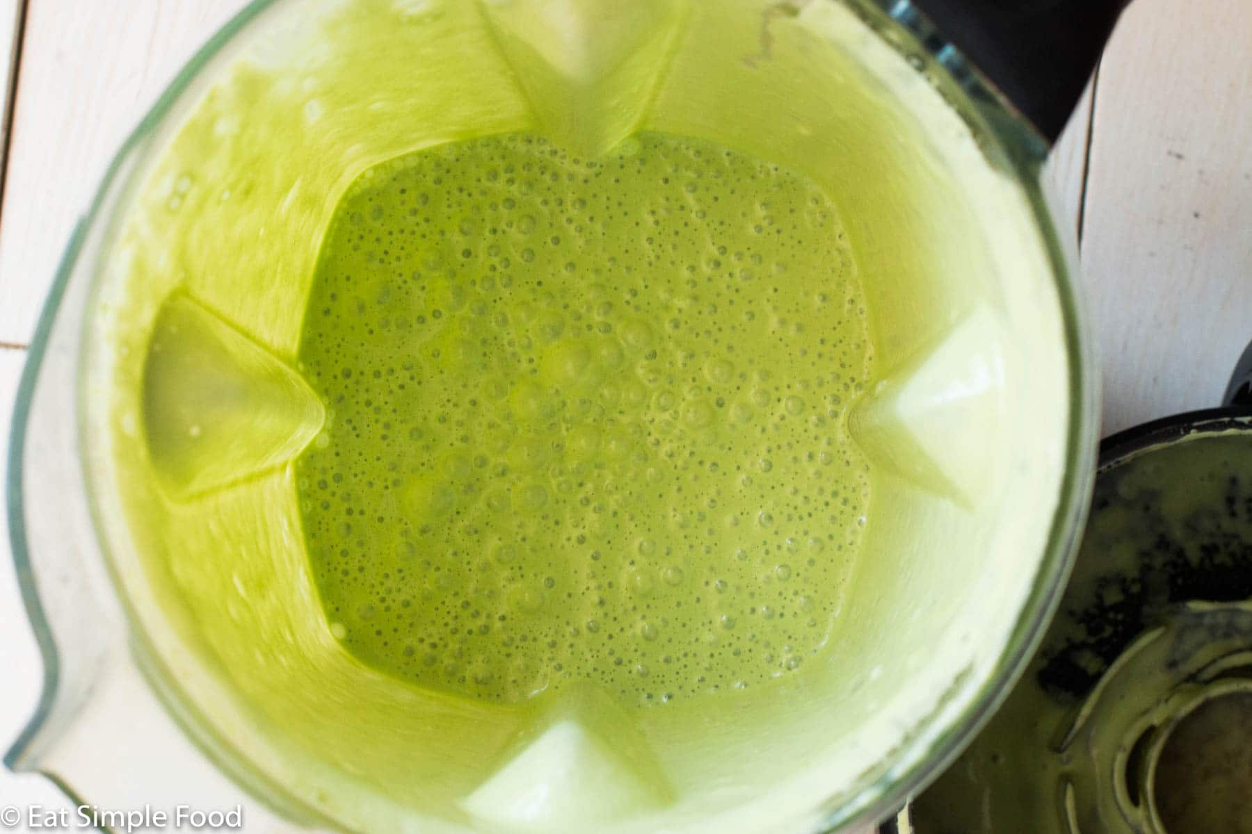 Top down view of a blender with pureed light green cilantro sauce.
