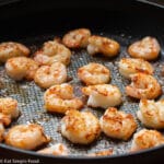 Crispy pan seared shrimp close up in a black pan with brown bits and fond stuck to the shrimp and pan. Closer up.