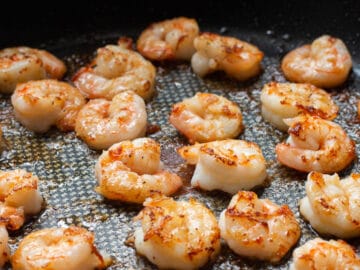 Crispy pan seared shrimp close up in a black pan with brown bits and fond stuck to the shrimp and pan. Closer up.
