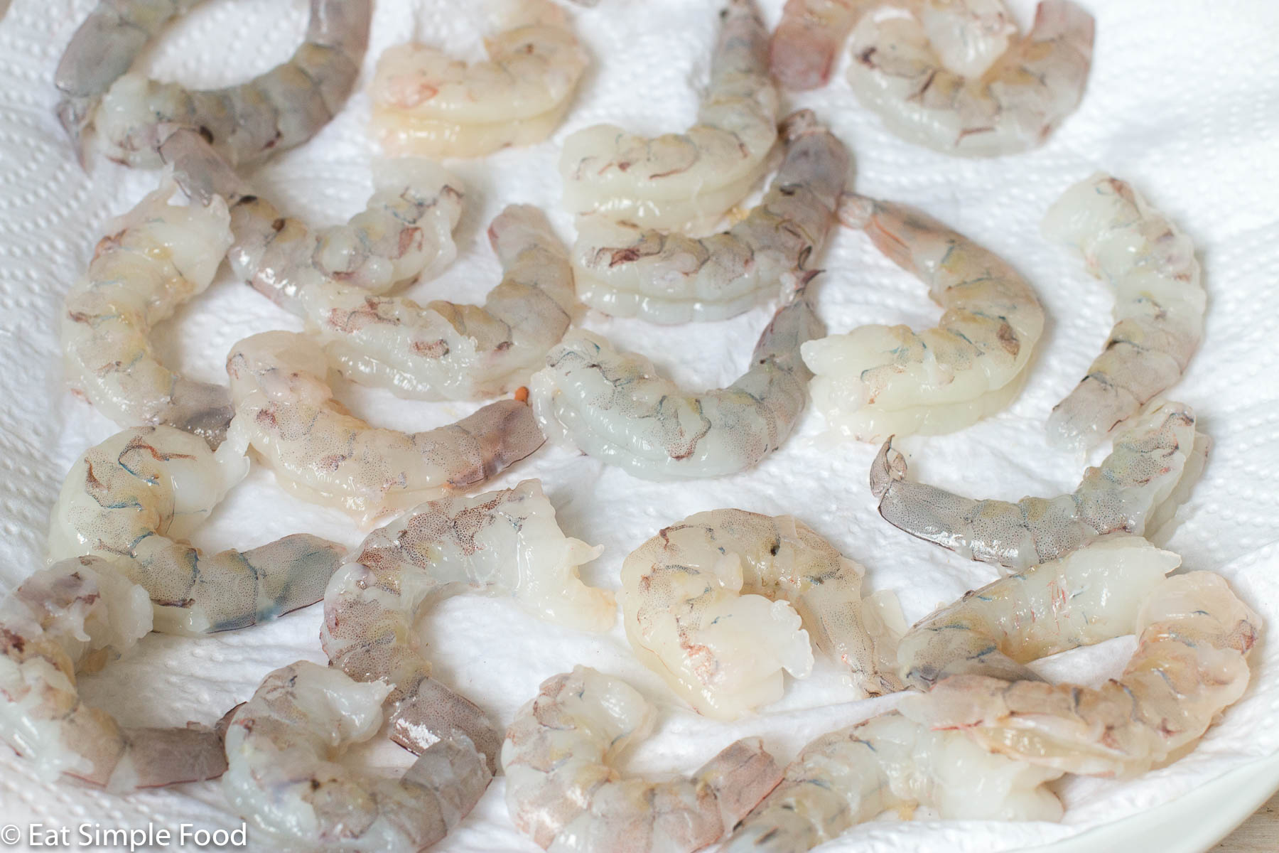 Peeled and deveined shrimp on a paper towel lined white plate. Close up.