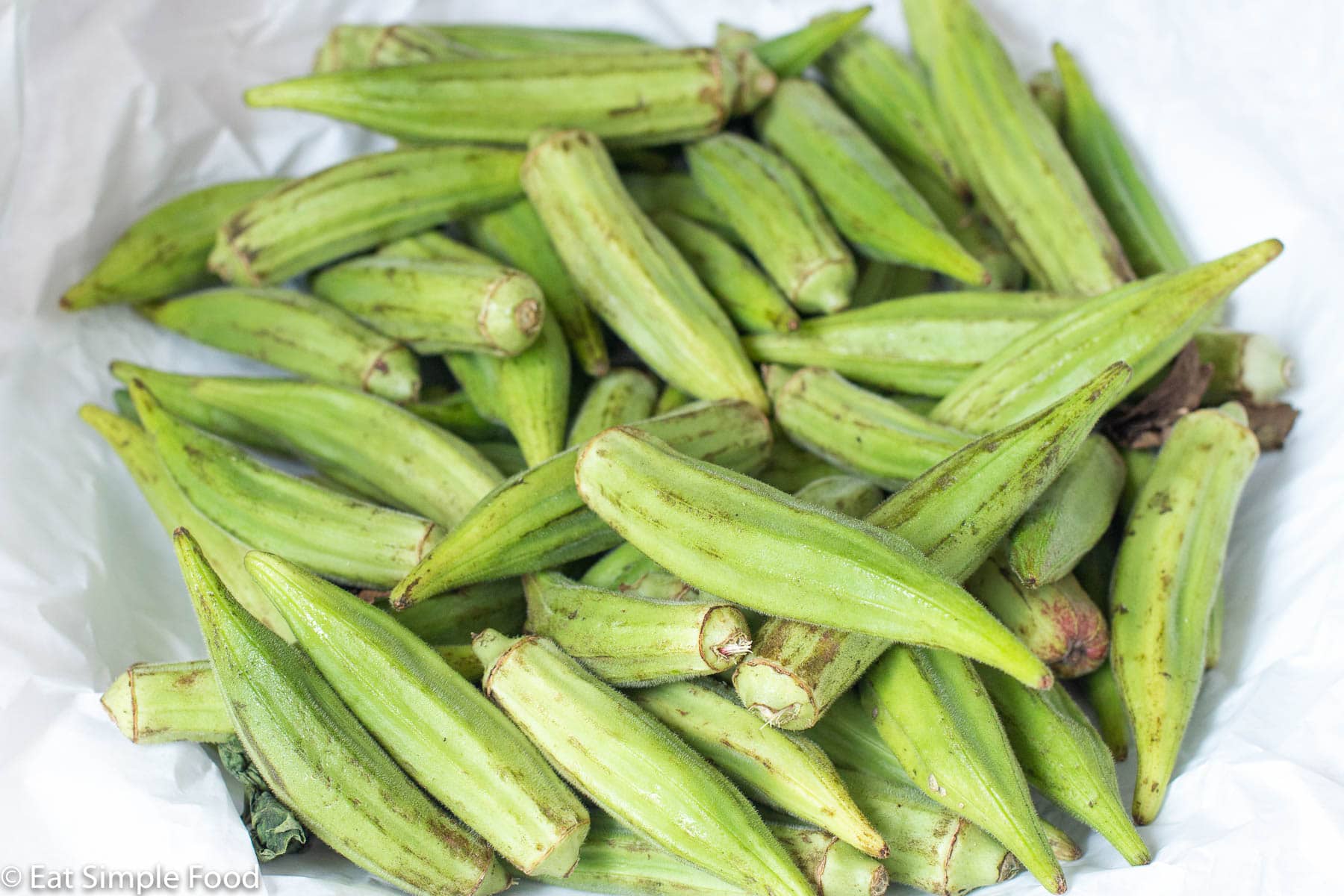 Whole fresh okra packed tightly on white lined parchment paper.