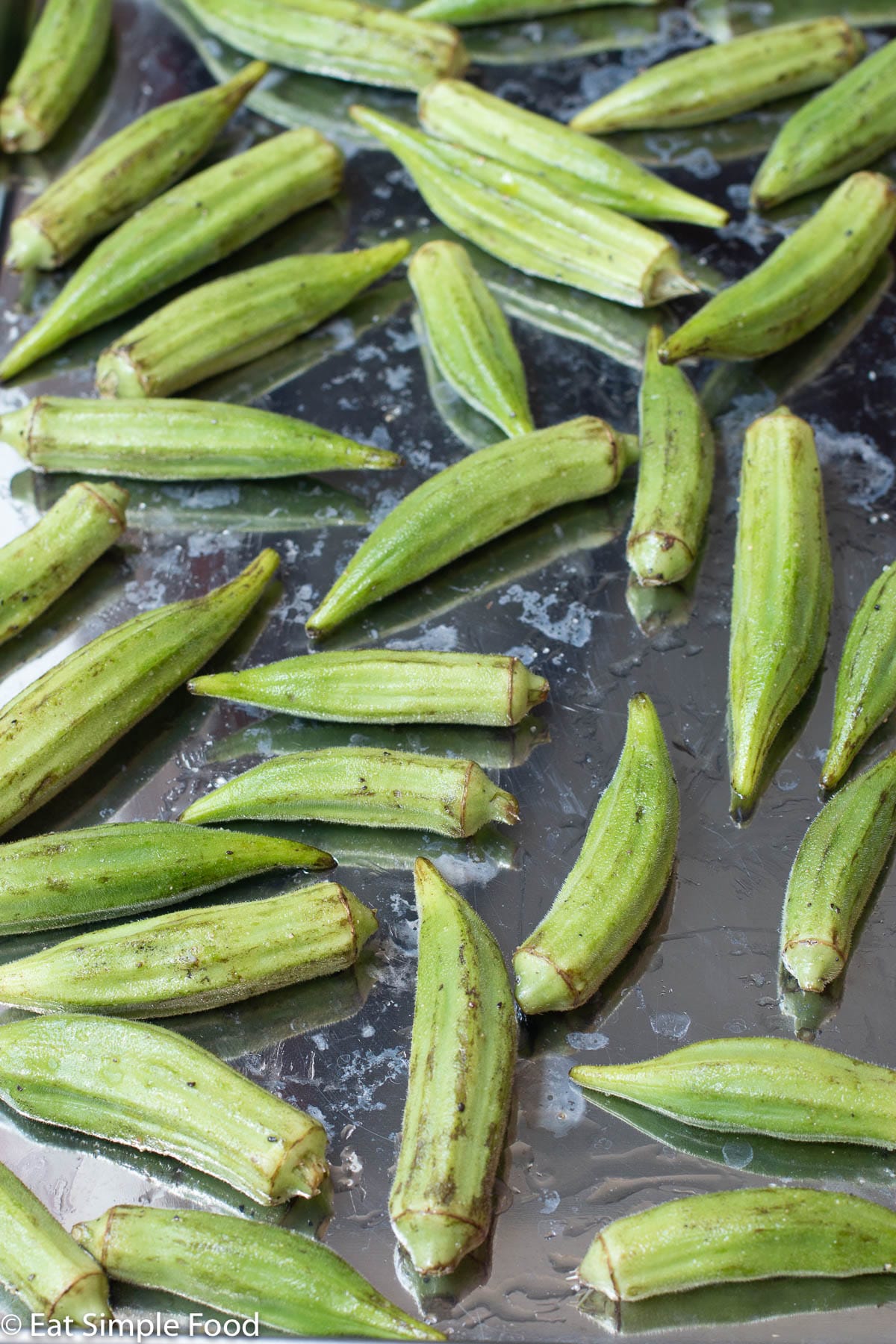 Raw whole okra laid on spaciously on a stainless steel baking sheet.