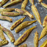 Raw whole okra laid on spaciously on a stainless steel baking sheet.