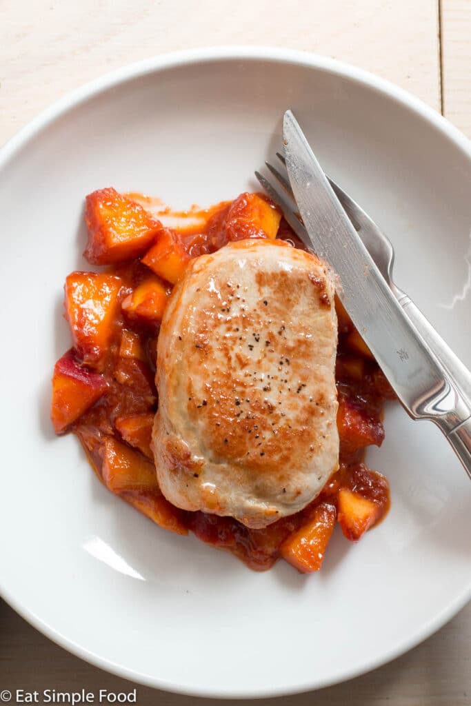 Top down view of a seared brown boneless pork chop over a peach tomato sauce on a white plate.
