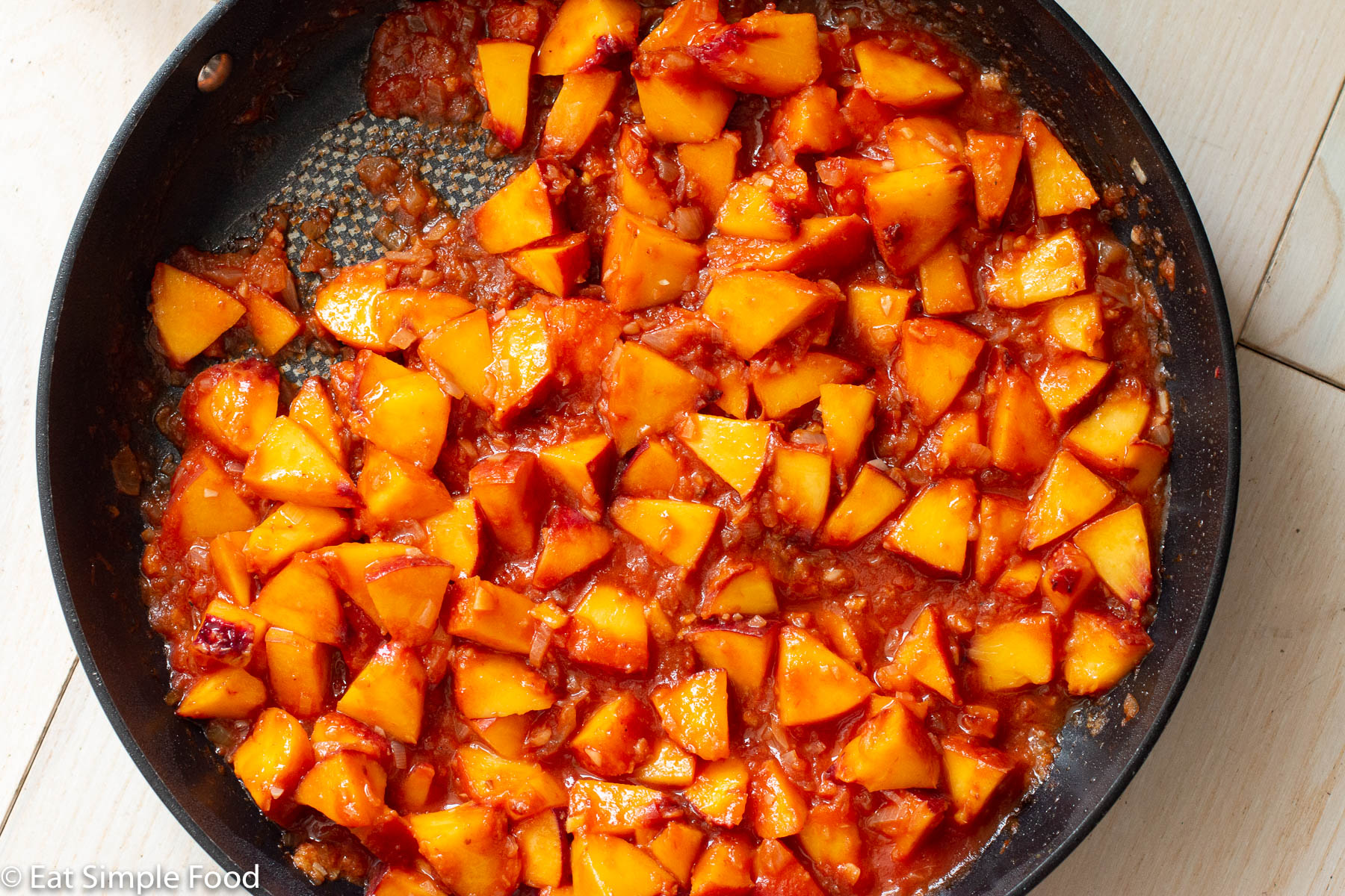Top down view of a black skillet with diced peaches in a tomato based sauce.