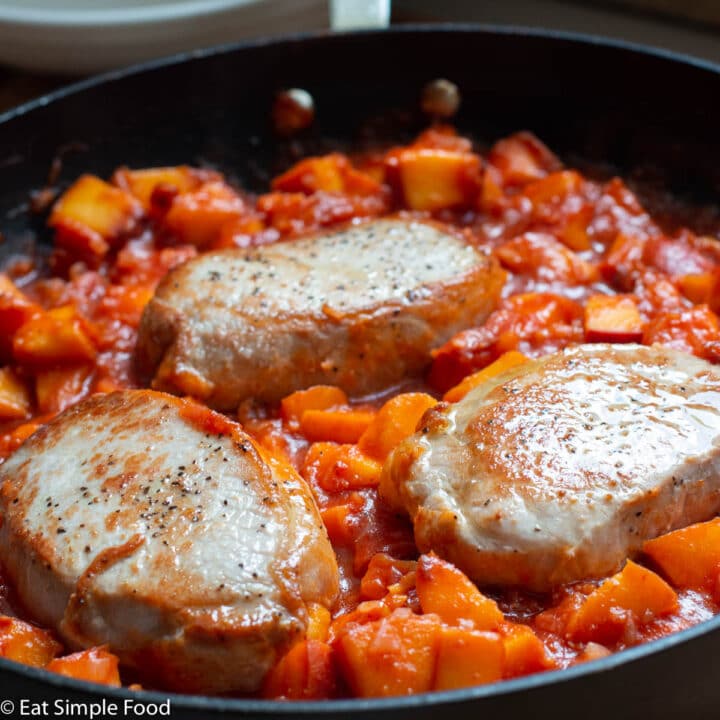 Side view of three boneless pork chops in a peach tomato sauce in a black skillet. Close up.