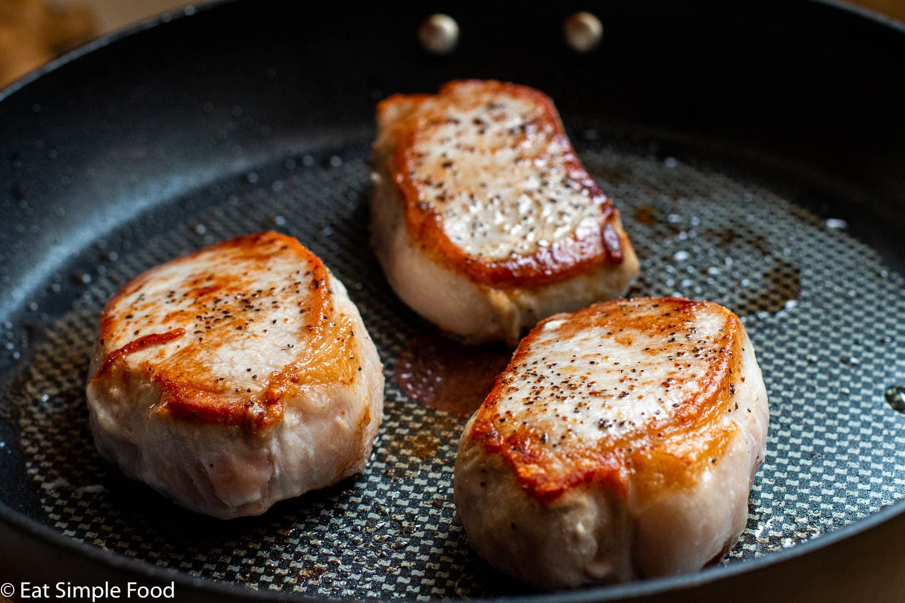 Three thick boneless pork chops seared brown in a black skillet.