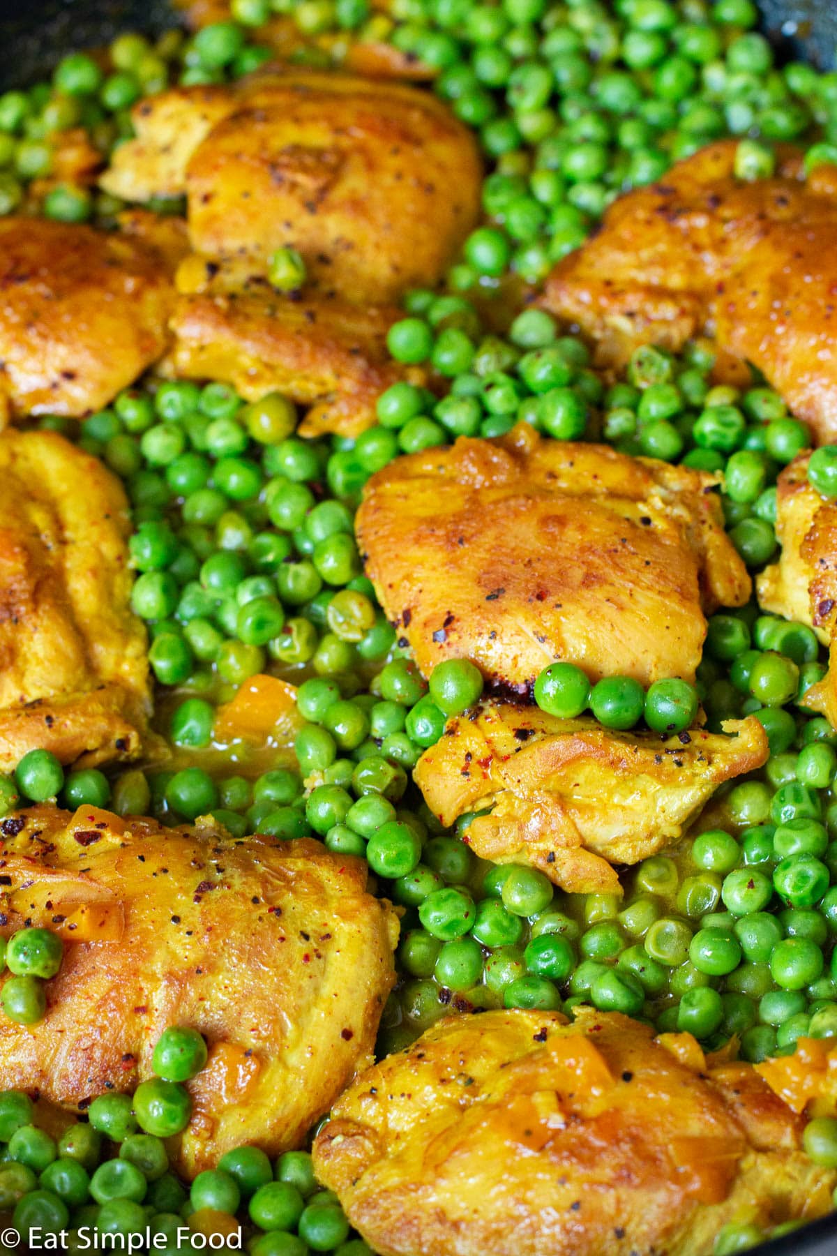 Browned boneless skinless chicken thighs on a bed of vibrant green peas. Side view. Close up.