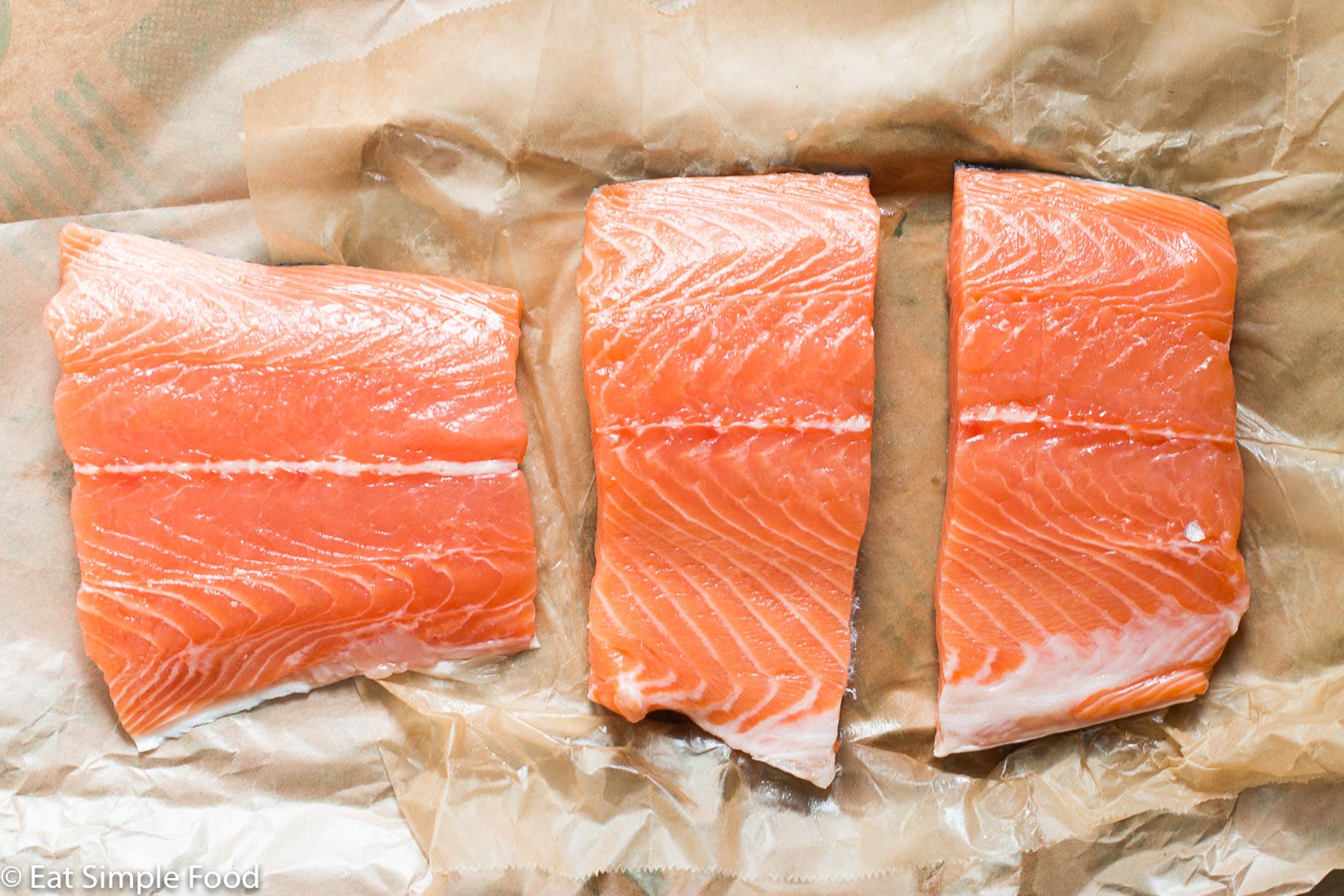 3 pieces of raw salmon fillets on butcher paper. Top down view.