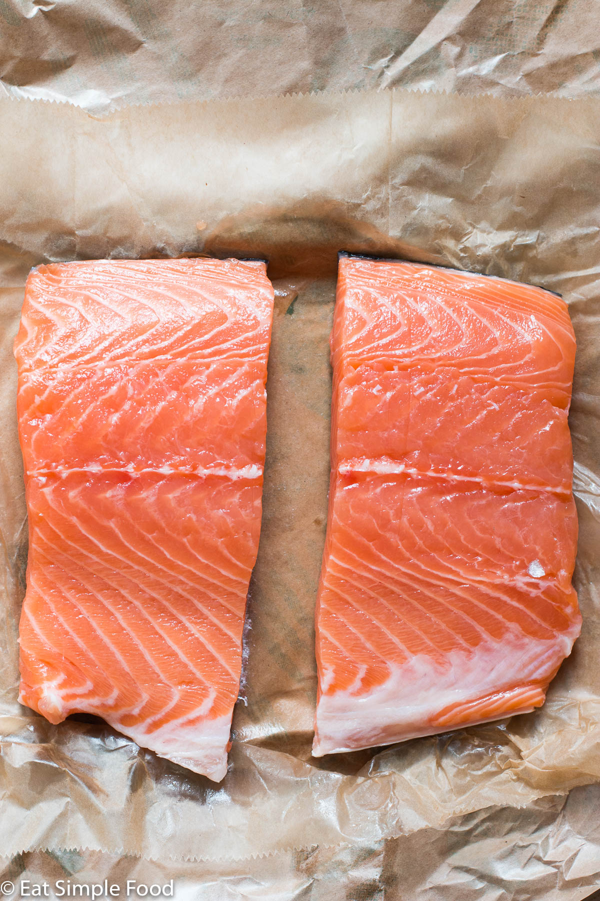 2 pieces of pink raw salmon on butcher paper. Top down view.