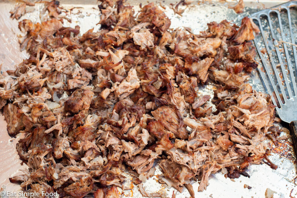 Close up side view of cooked crispy pork carnita bits on a sheet pan with a fish spatula on the side.