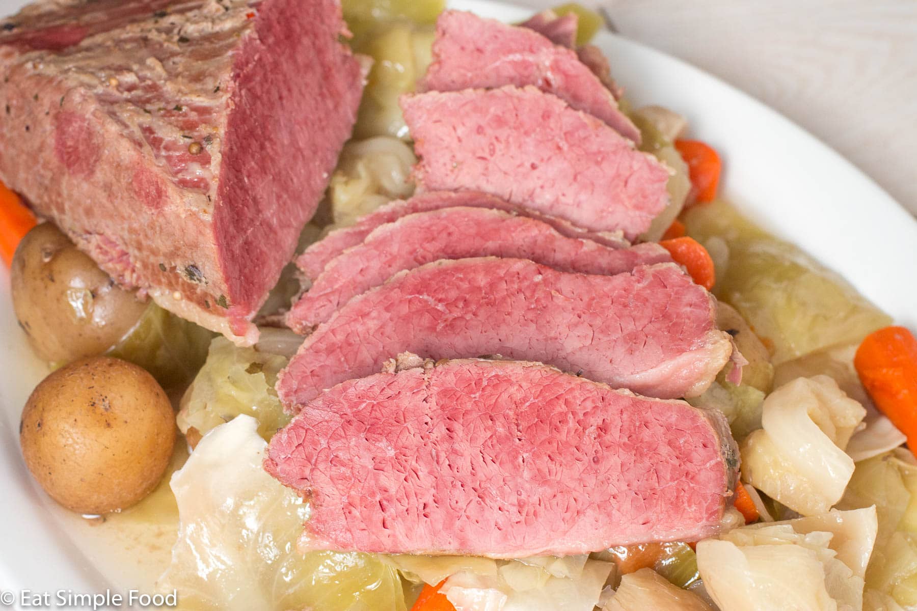 Side view of layered thin sliced cooked corned beef on cabbage on a white plate.