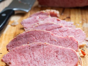 Close up of thin sliced pink corned beef on a wood cutting board.