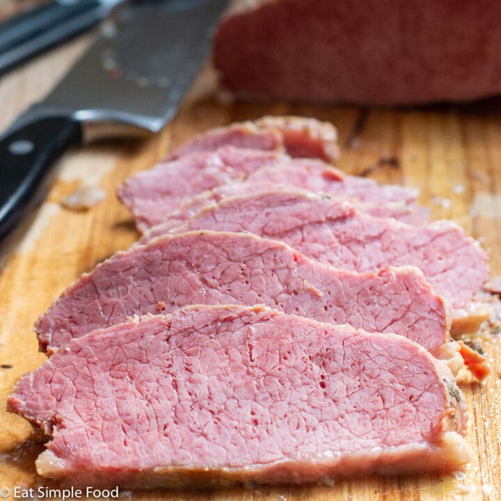 Close up of thin sliced pink corned beef on a wood cutting board.