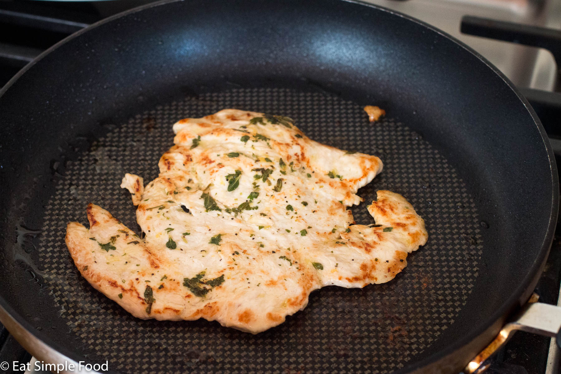 Flattened piece of chicken breast seared in a black skillet. Side view.