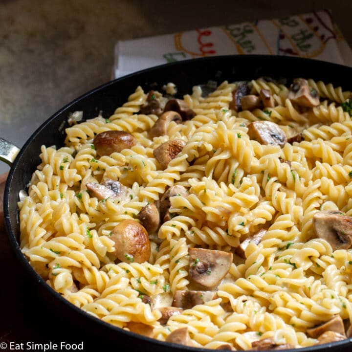 Close up of pan of fusilli pasta with quartered mushrooms in a light cream sauce with parsley garnish.
