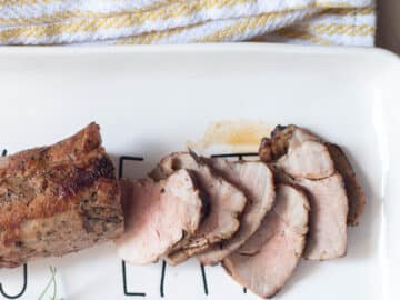 Seared and thinly sliced pork tenderloin. Top view on a white plate with a sprig of rosemary in the background.