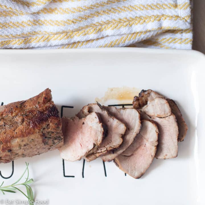 Seared and thinly sliced pork tenderloin. Top view on a white plate with a sprig of rosemary in the background.