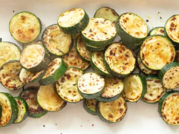 Seared and browned caramelized sliced zucchini rounds on a white plate with red pepper flakes lightly garnished. Top view crop to a rectangle.