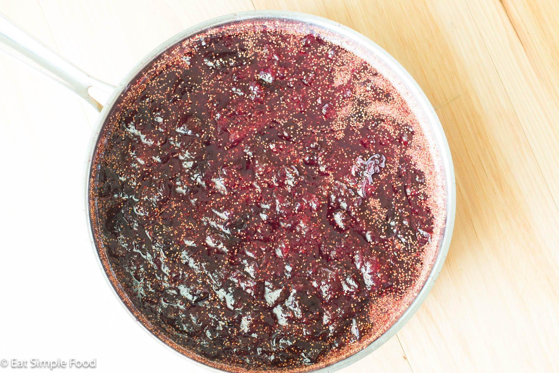 Top down view of cherry red fig jam with seeds in a stainless steel pot.