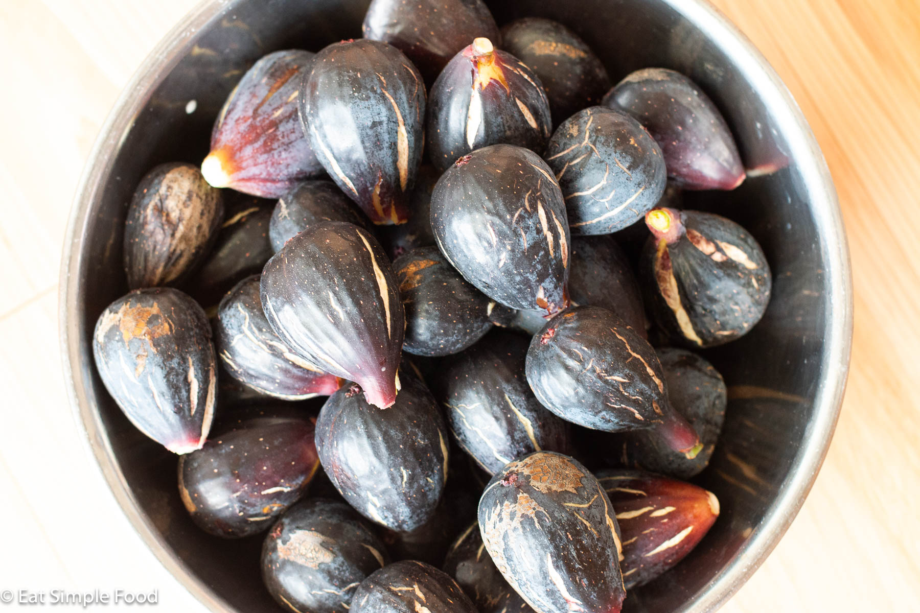 Top down view of a stainless steel bowl full of ripe figs.