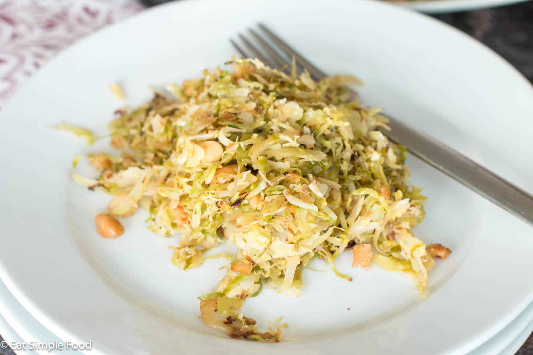 White plate with fork of shaved Brussels sprouts and almonds. White and purple napkin in background.